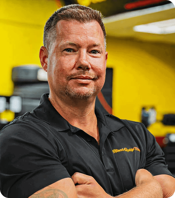 Self-confident man in black uniform with arms crossed in car repair shop, representing United Franchise Group automotive franchise opportunities and business growth.